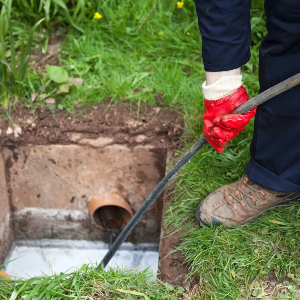 Photo montrant des mains et pieds équipés de gants et bottes utilisant un deboucheur assainisseur dans un pack chemisage de canalisation